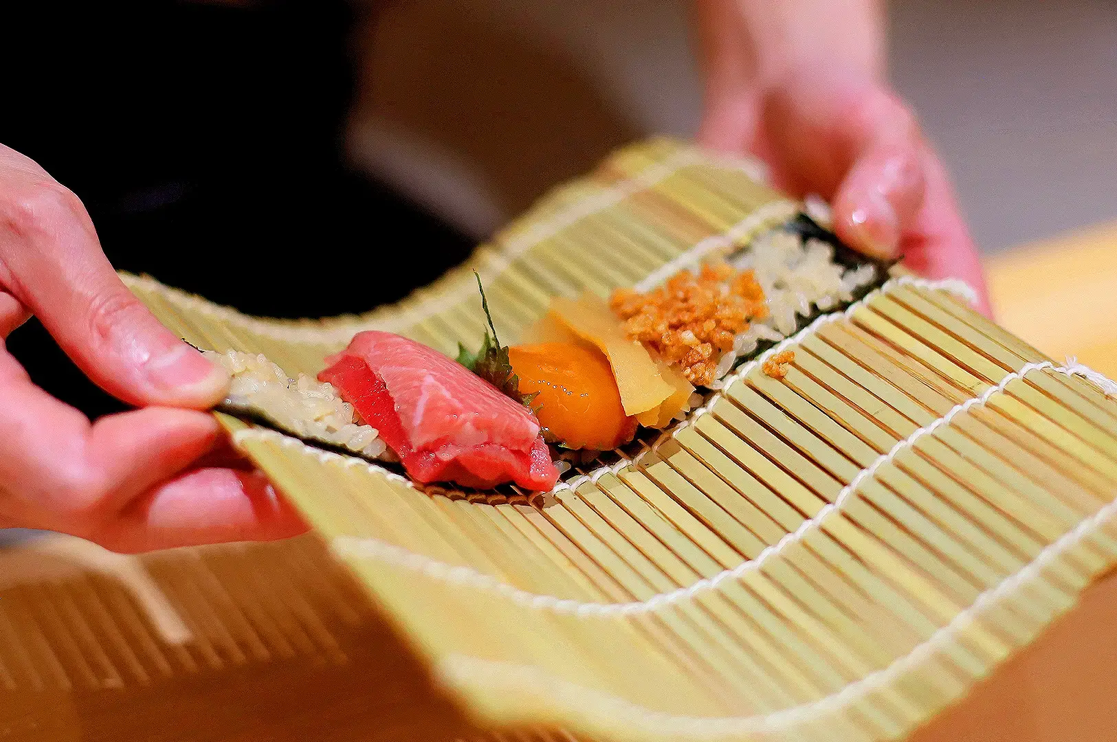 Omakase sushi chef preparing fresh nigiri with premium tuna, uni and seafood on a traditional bamboo sushi mat in Singapore