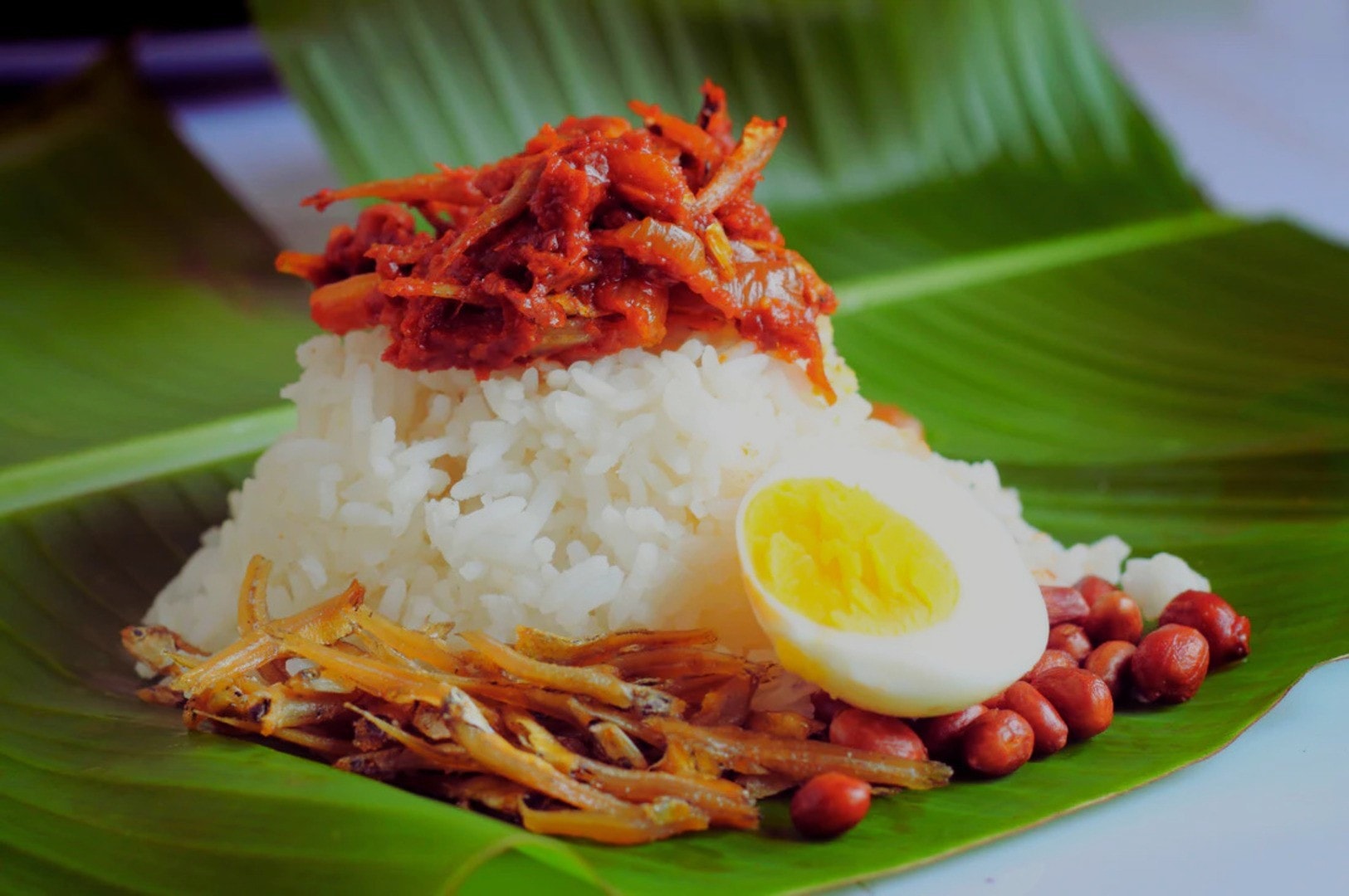 Nasi Lemak served on a banana leaf, showcasing rice, beans, and a sunny-side-up egg on a decorative plate.