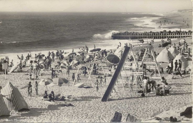 Vintage photograph of Hossegor beach filled with people enjoying the sun and sea, with beach umbrellas, play structures, and tents. The Atlantic Ocean waves can be seen in the background, capturing the lively atmosphere of Hossegor in the past.