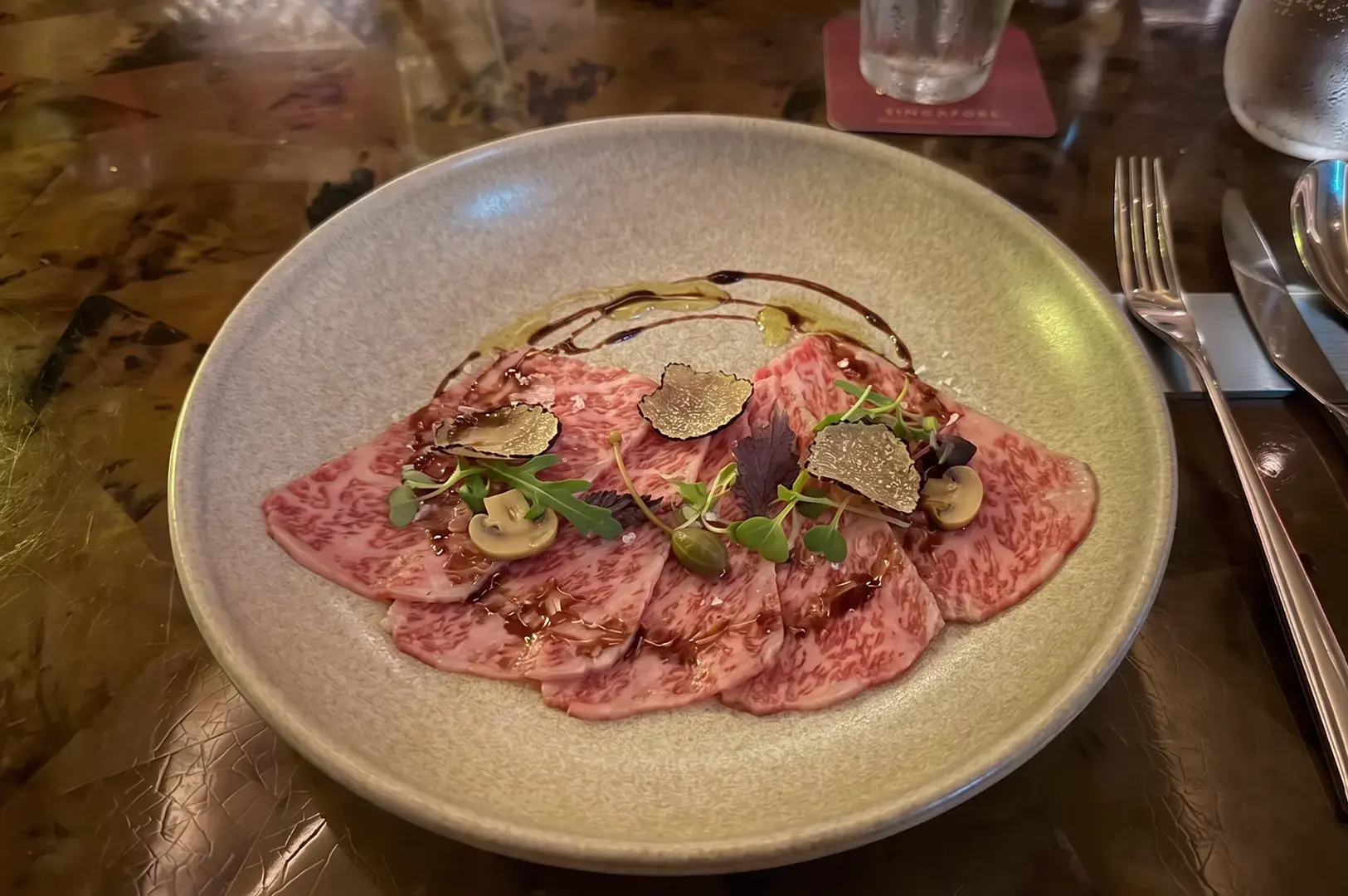 A gourmet plate of thinly sliced Wagyu beef carpaccio topped with fresh black truffle shavings and microgreens.