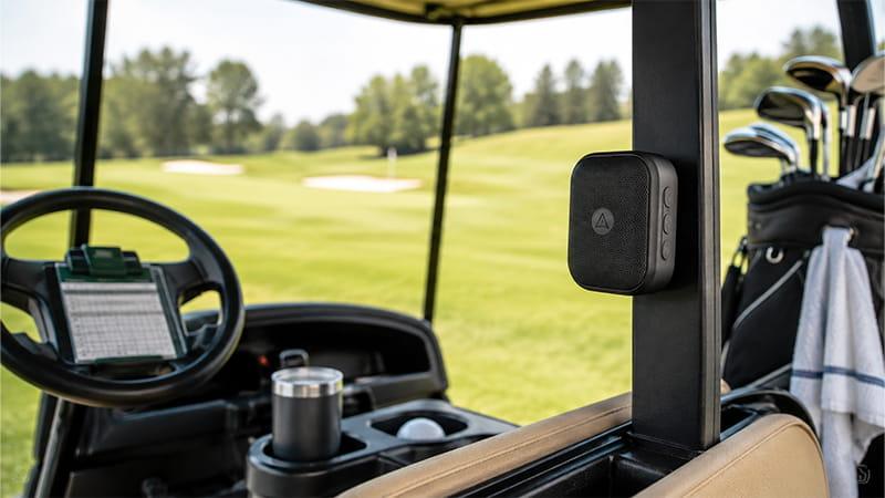 Magnetic golf cart speaker attached to a cart frame with golf clubs and a golf course in the background