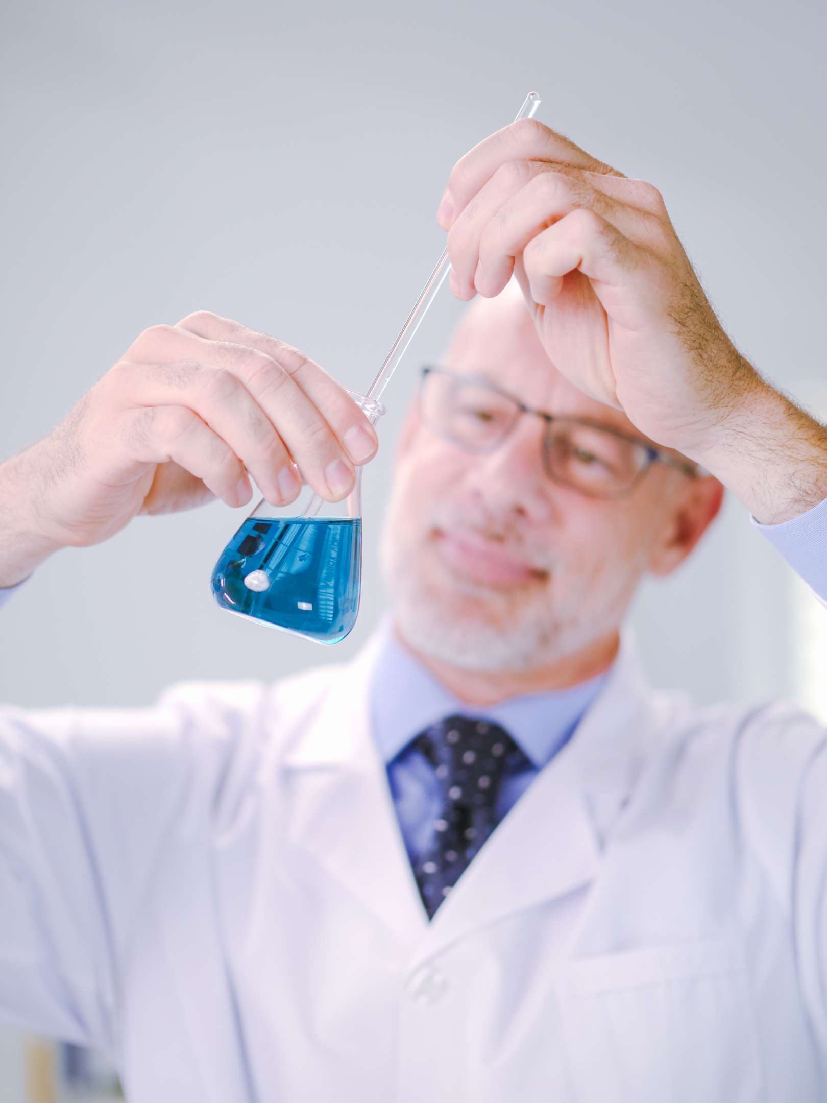 man in white coat stirring blue liquid in a laboratory flask