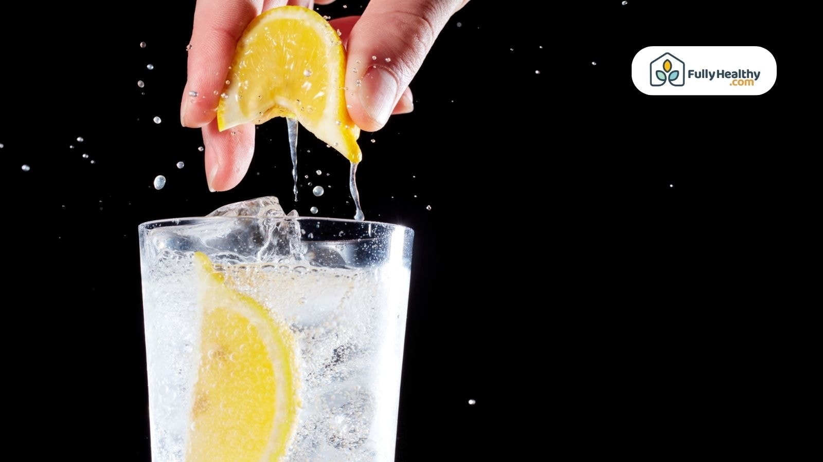 Hand squeezing lemon half into glass of sparkling water splash effect