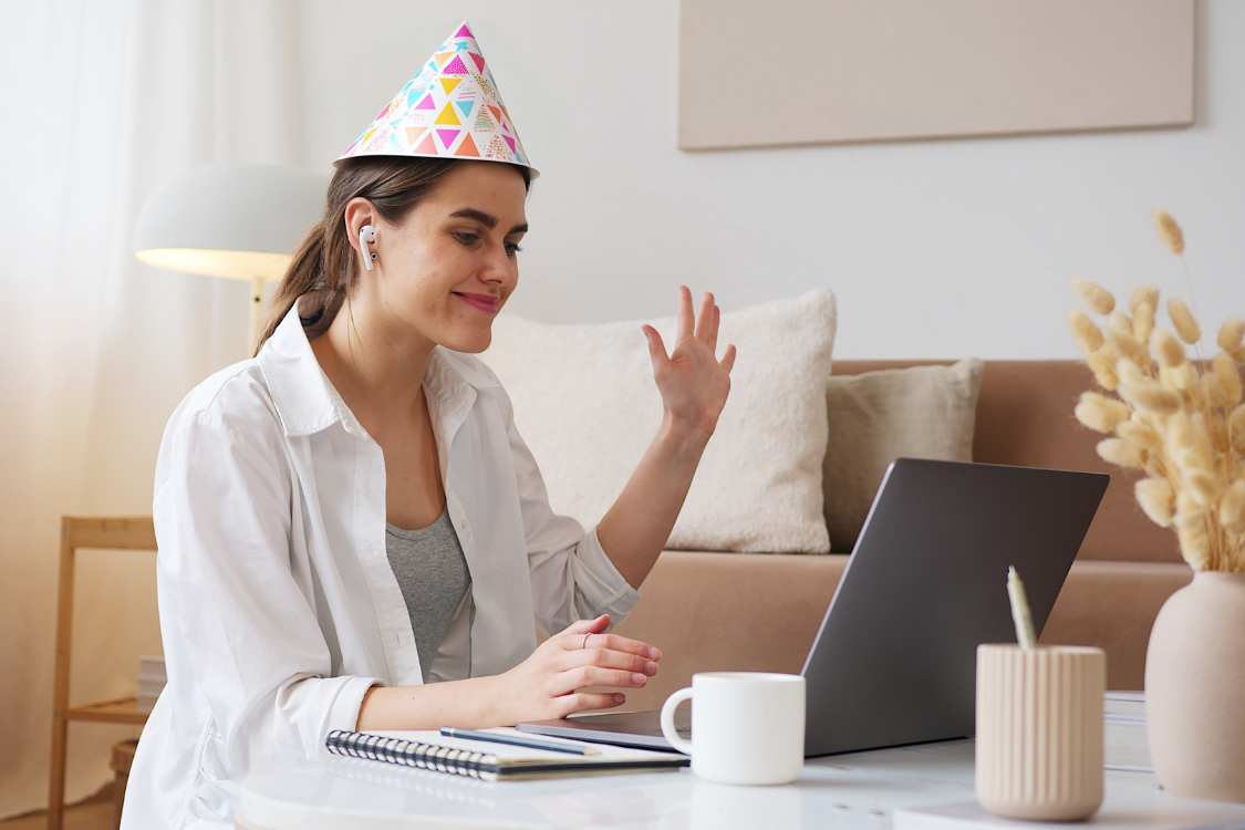 Remote employee wearing a party hat and smiling during virtual meeting, showing team celebration and appreciatio