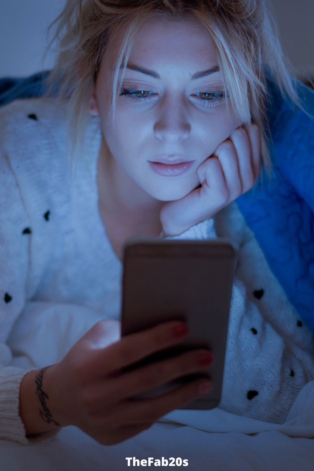 Woman under covers checking phone