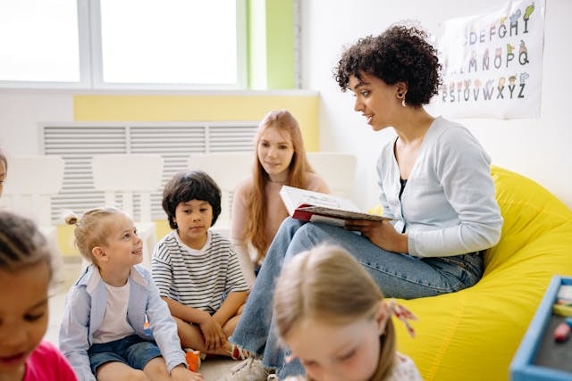 Woman seated in a yellow beanbag reading a book to children