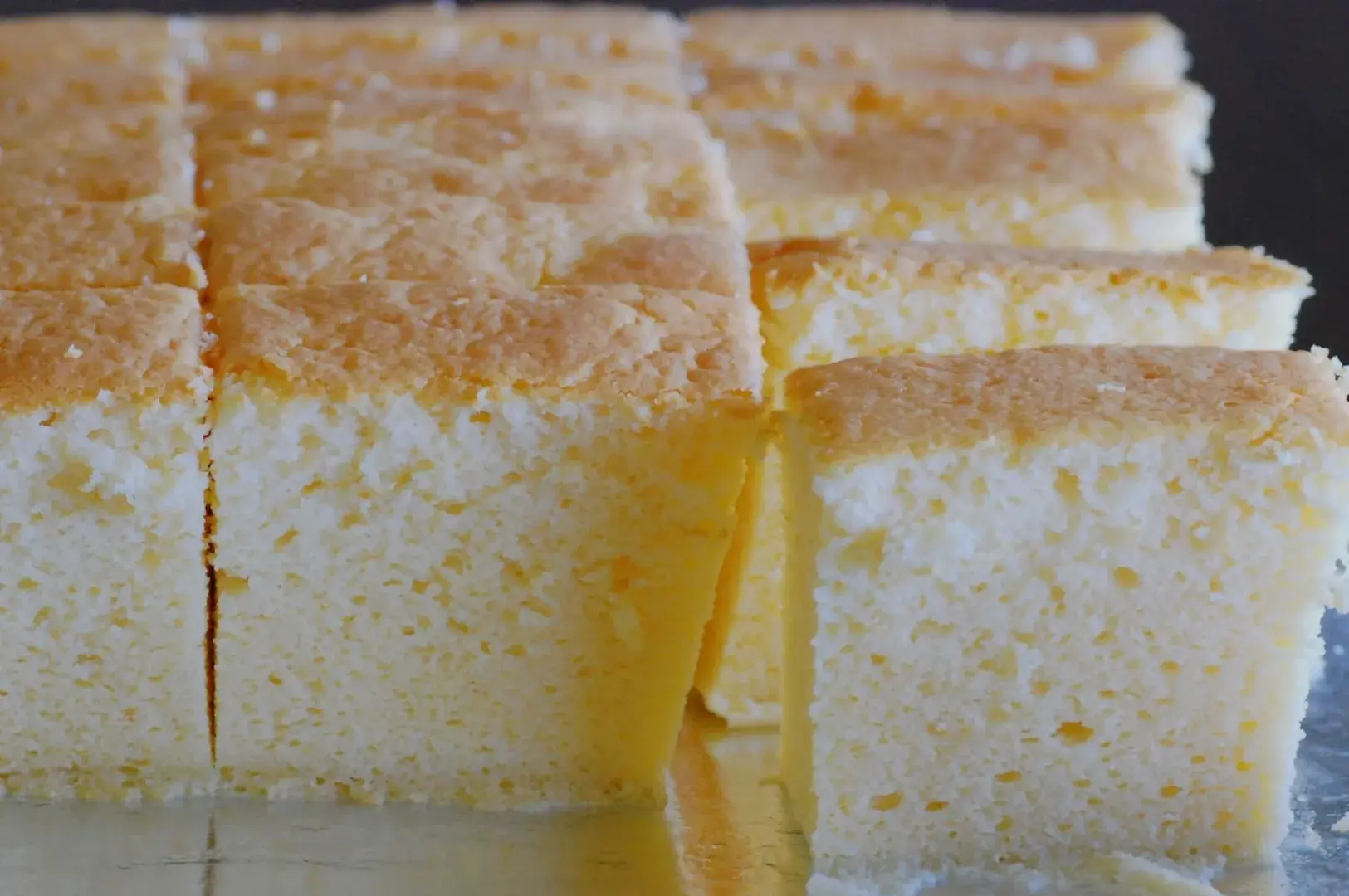 A close-up of a freshly baked cake, cut into squares, showcasing its light, fluffy texture.