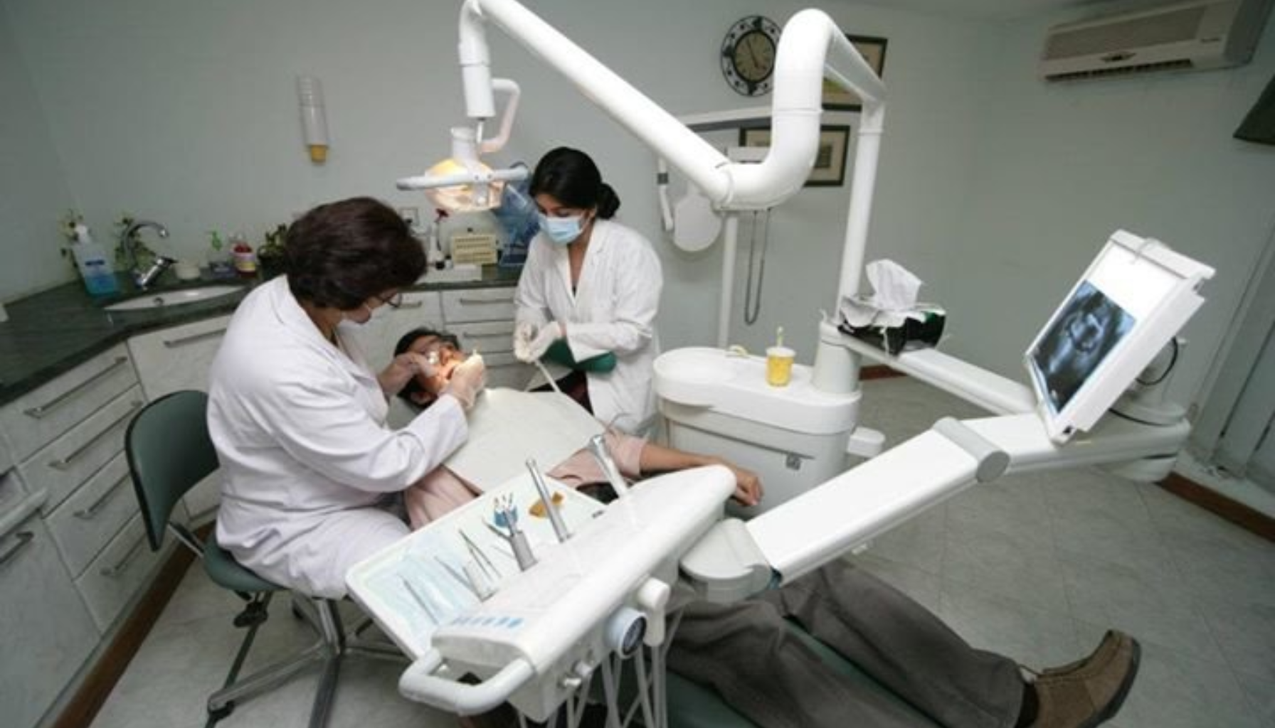 Tannleger behandler pasient i moderne tannlegeklinikk med avansert utstyr og skjerm som viser røntgenbilde.
