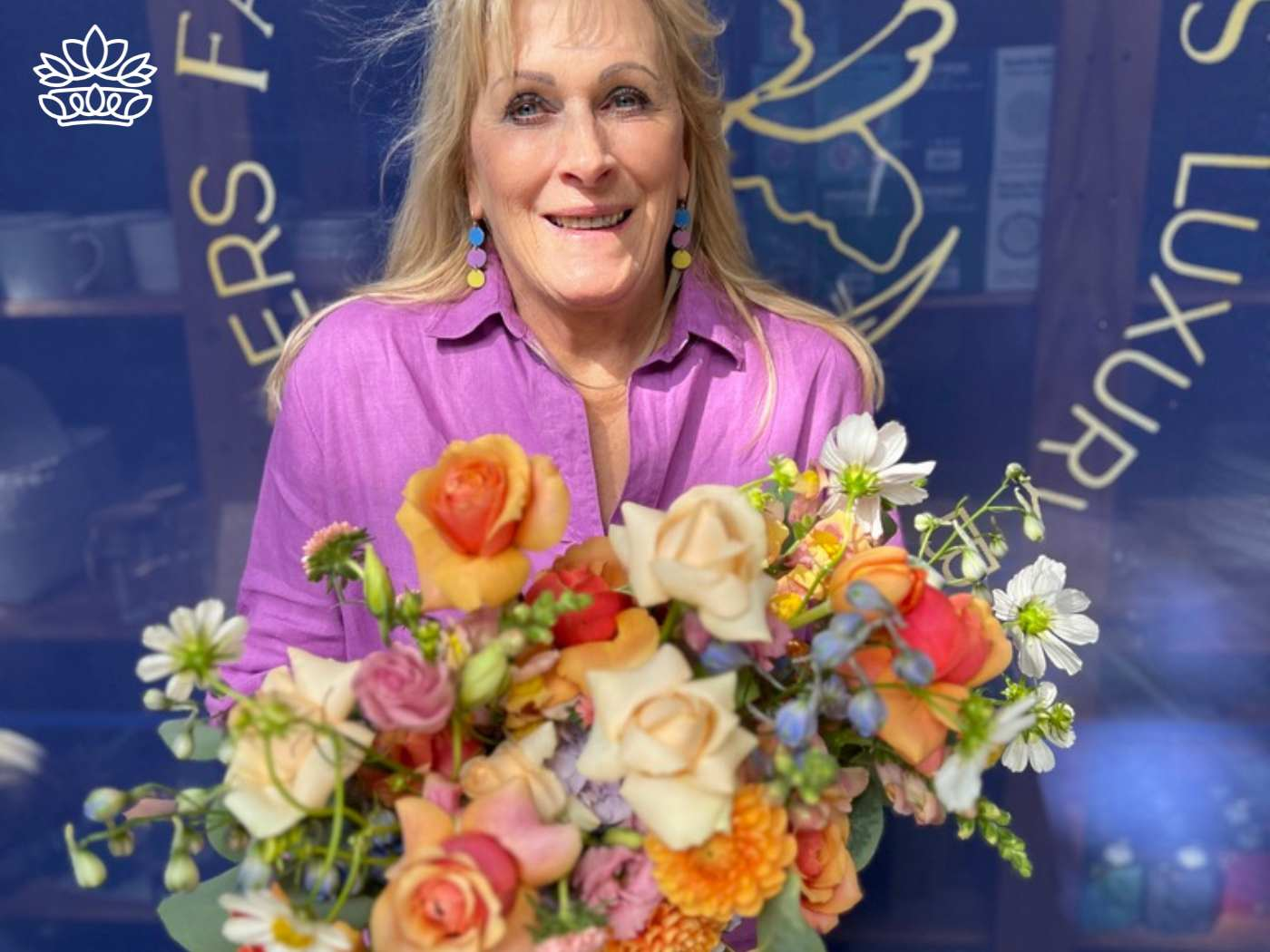 A cheerful florist in a pink blouse, radiant as she presents a colourful bouquet of roses and wildflowers, symbolizing the vibrant selection from the Flowers By Occasion Collection at Fabulous Flowers and Gifts.
