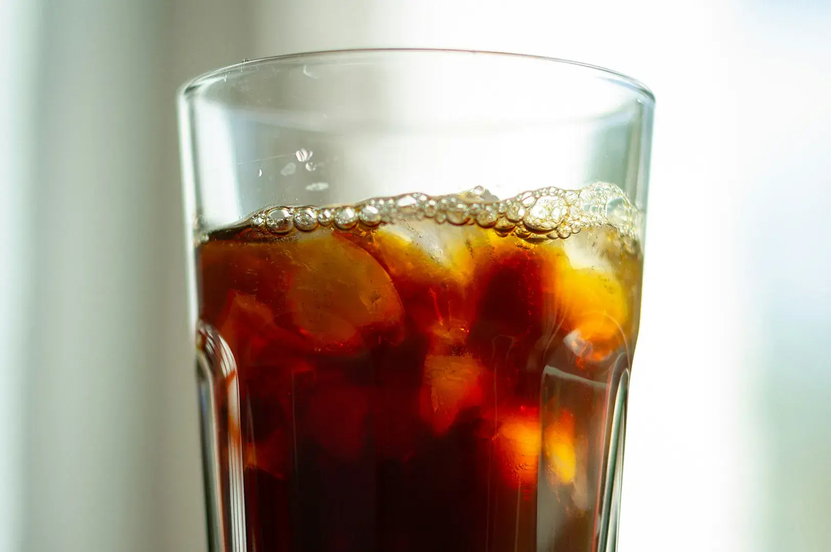 Eye-level close-up shot of a tall glass of iced tea filled with black tea, ice, and a layer of foam on top.