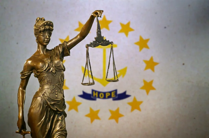 Lady Justice holding imbalanced scale with State of Rhode Island flag background