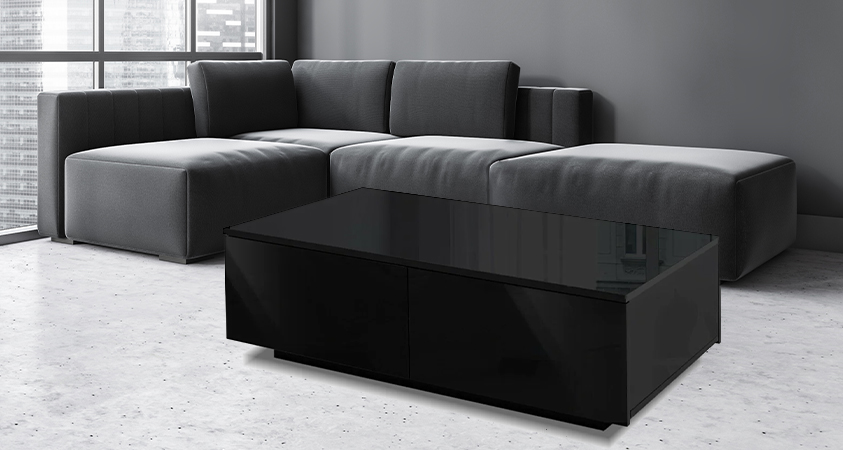An Artiss 4-drawer black high-gloss coffee table, set in a greyscale living room in front of a grey leather sectional sofa. A cityscape can be seen through a window in the background