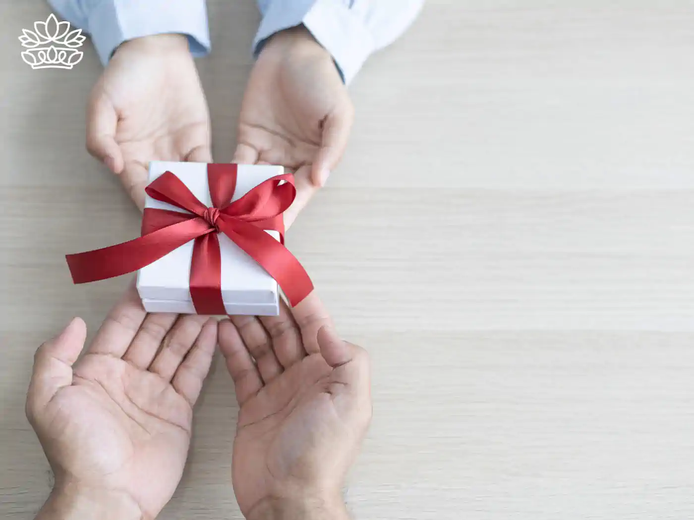 Close-up of two hands presenting a small white gift box with a vibrant red ribbon, symbolizing a thoughtful and personal gesture. Teachers & Educators Gift Boxes. Delivered with Heart. Fabulous Flowers and Gifts