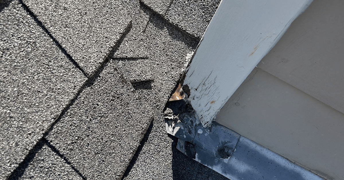 Damaged flashing and deteriorated wood trim at the base of a roof line, showing signs of water infiltration.