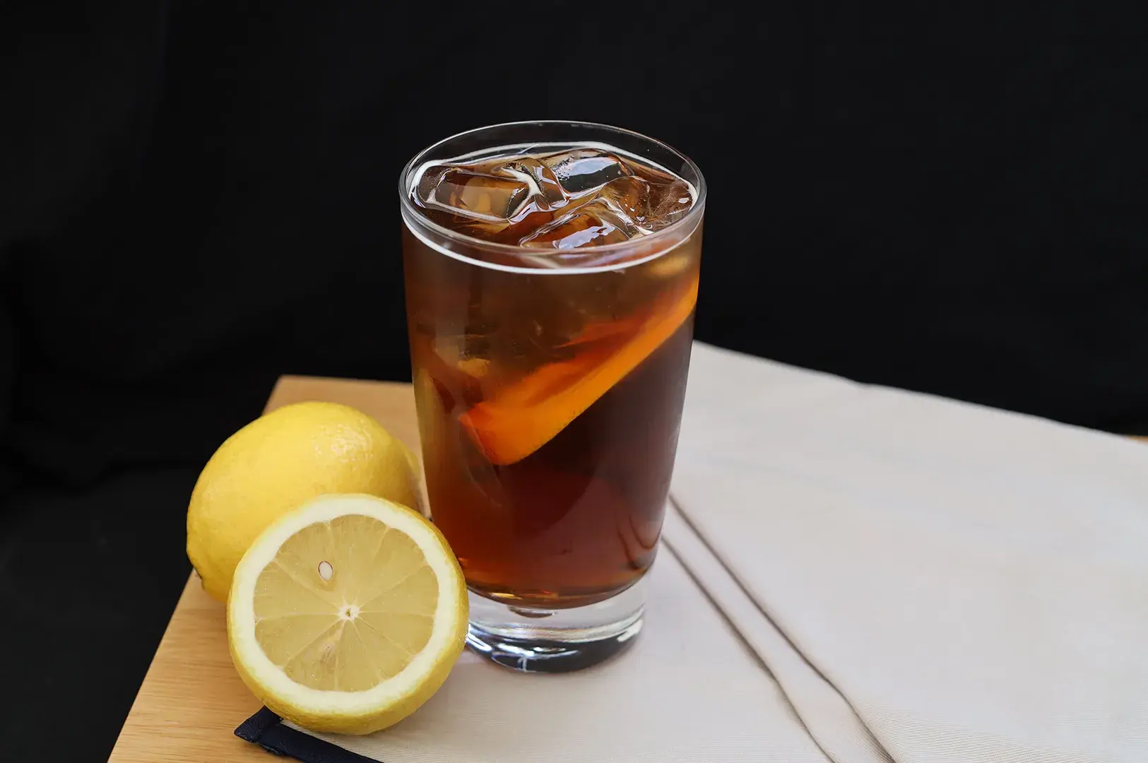 Glass of iced lemon tea served with fresh lemons on a wooden surface.