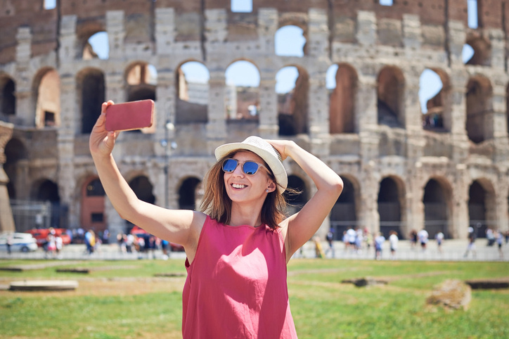 Happy young woman taking a selfie in front of the Coliseum in Rome.