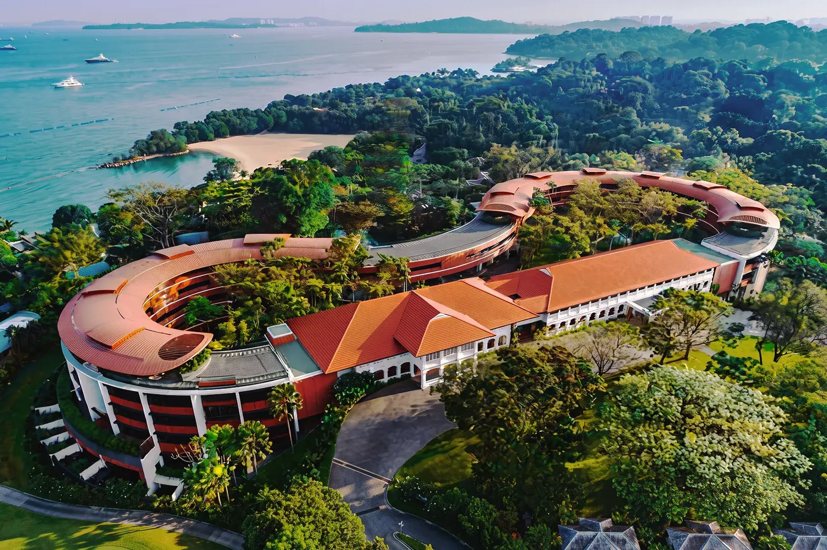 Aerial view of luxury beachfront resort in Singapore surrounded by tropical greenery and overlooking the sea.