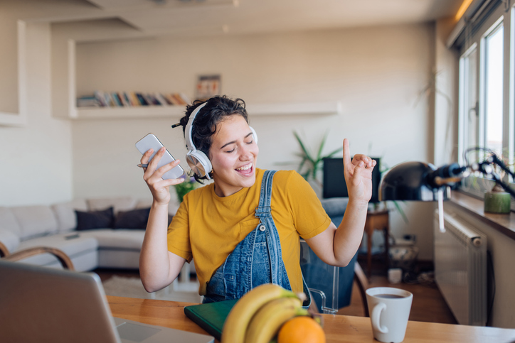 Cheerful young woman listening to music and singing along on her iPhone 15.