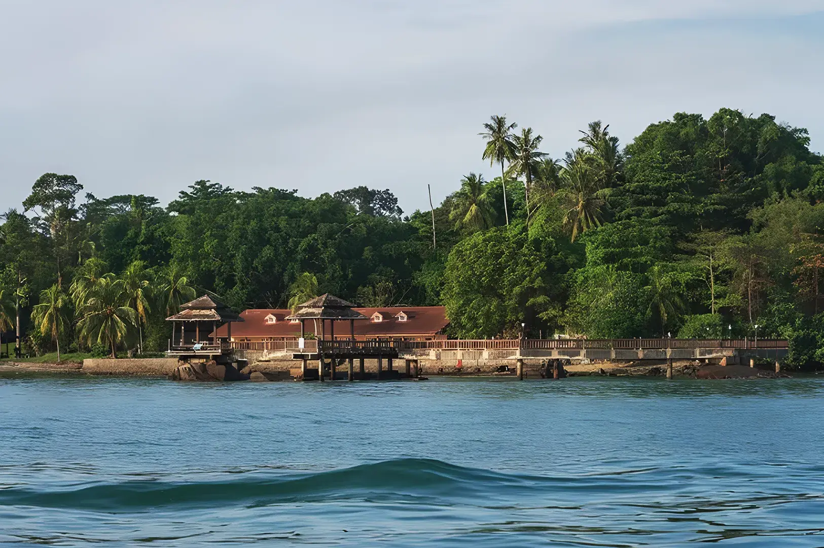 Pulau Ubin waterfront lodge surrounded by tropical trees and wooden pavilions overlooking calm blue sea in Singapore