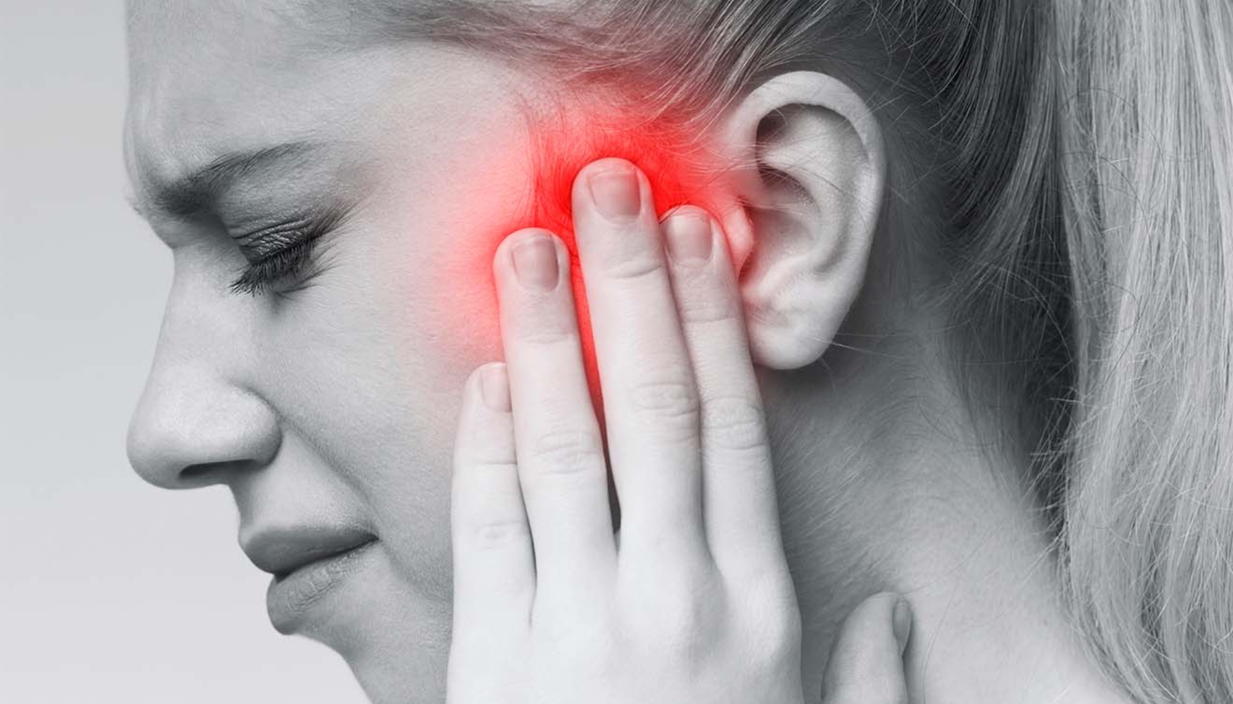 Kvinne med smertefullt uttrykk holder hånden mot øret og kinnet, med rødhet som illustrerer intens nevralgisk smerte.