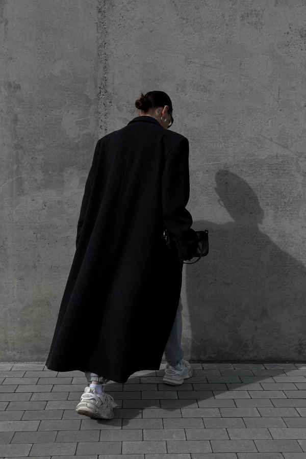 a woman in a large black coat and sneakers