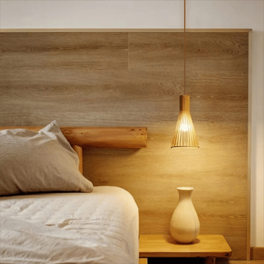 Japandi-style pendant light with a woven wooden shade, hanging beside a wooden bed frame in a minimalist bedroom, creating a warm, serene ambiance with natural textures.