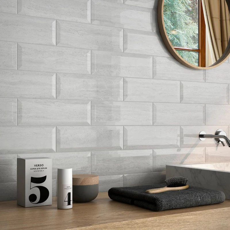 Glossy light grey bevelled wall tiles in a horizontal brick pattern behind a modern vanity with minimalist accessories.