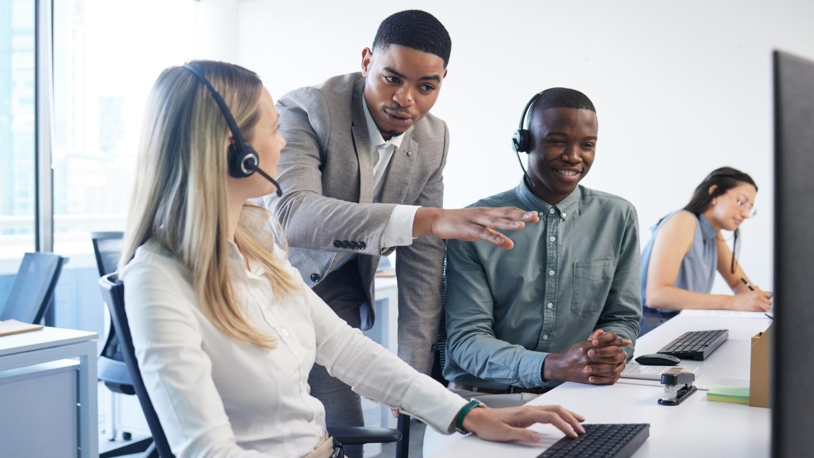A manager is coaching a call center support team in front of their computer work stations.