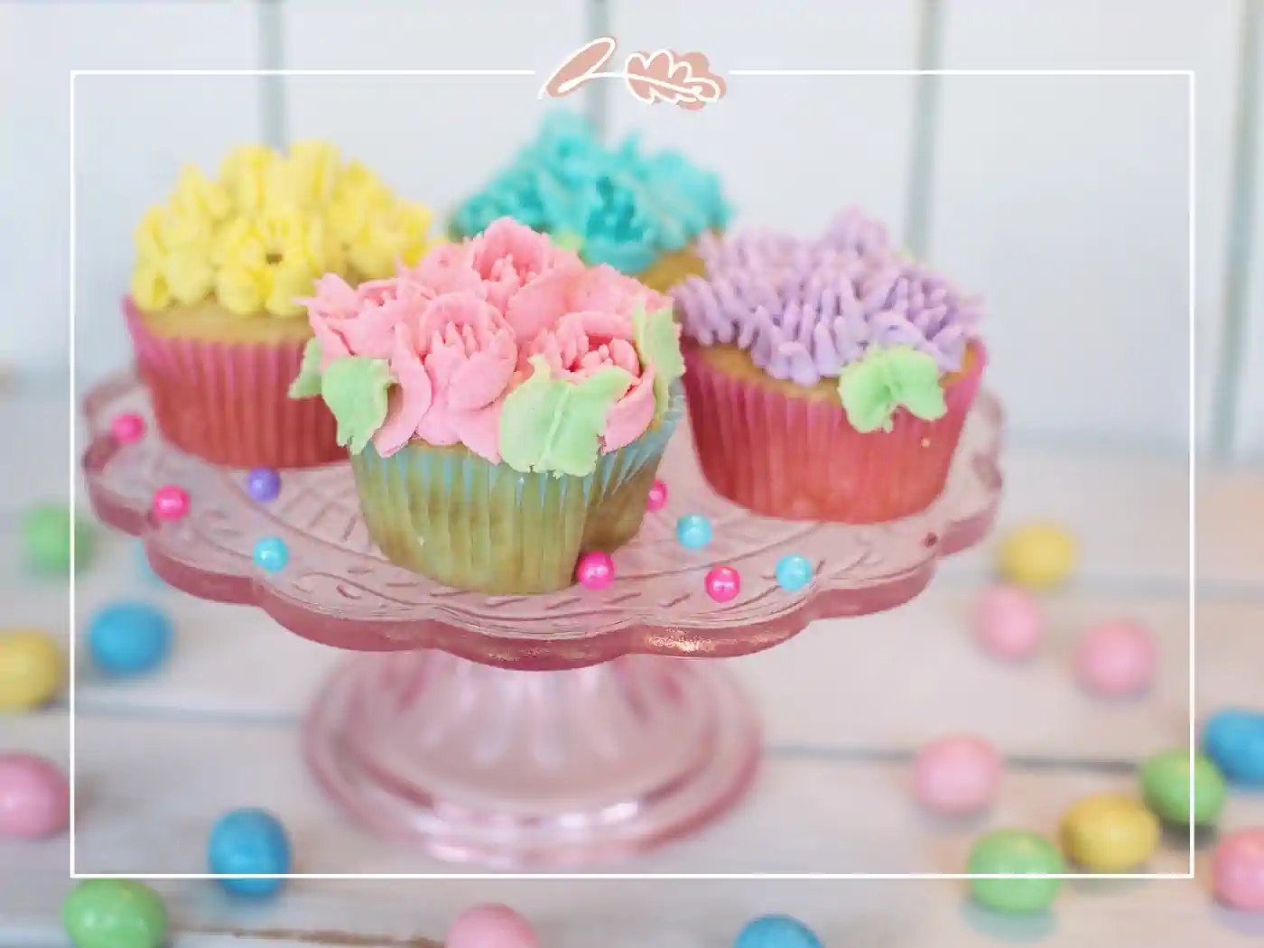 A display of colorful cupcakes adorned with intricate floral icing on a pink cake stand. Fabulous Flowers and Gifts - Birthday Collection.