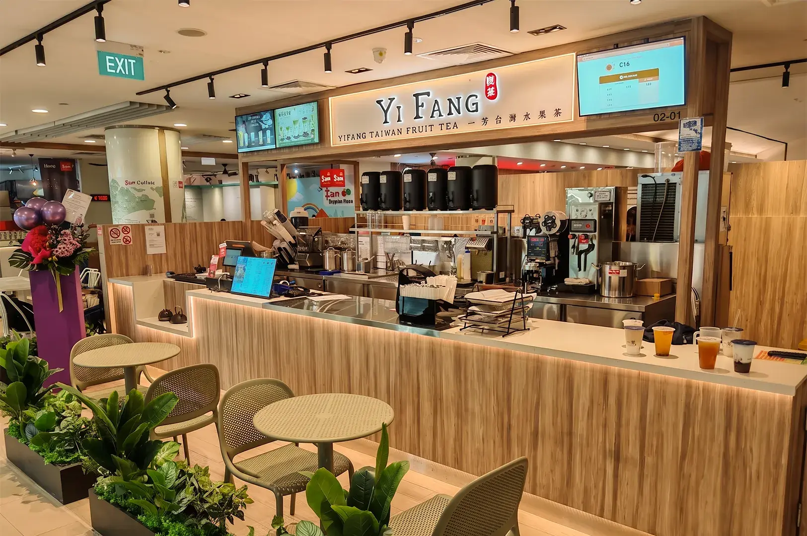 Storefront of a Yi Fang Taiwan Fruit Tea shop with a wooden service counter, digital menu boards, and small seating area.