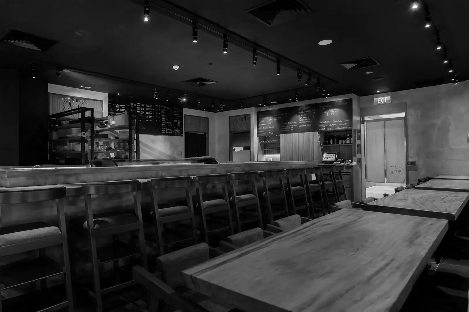 Cozy interior of Koji Sushi Bar at Raffles City featuring a sushi counter, wooden tables, and warm lighting.