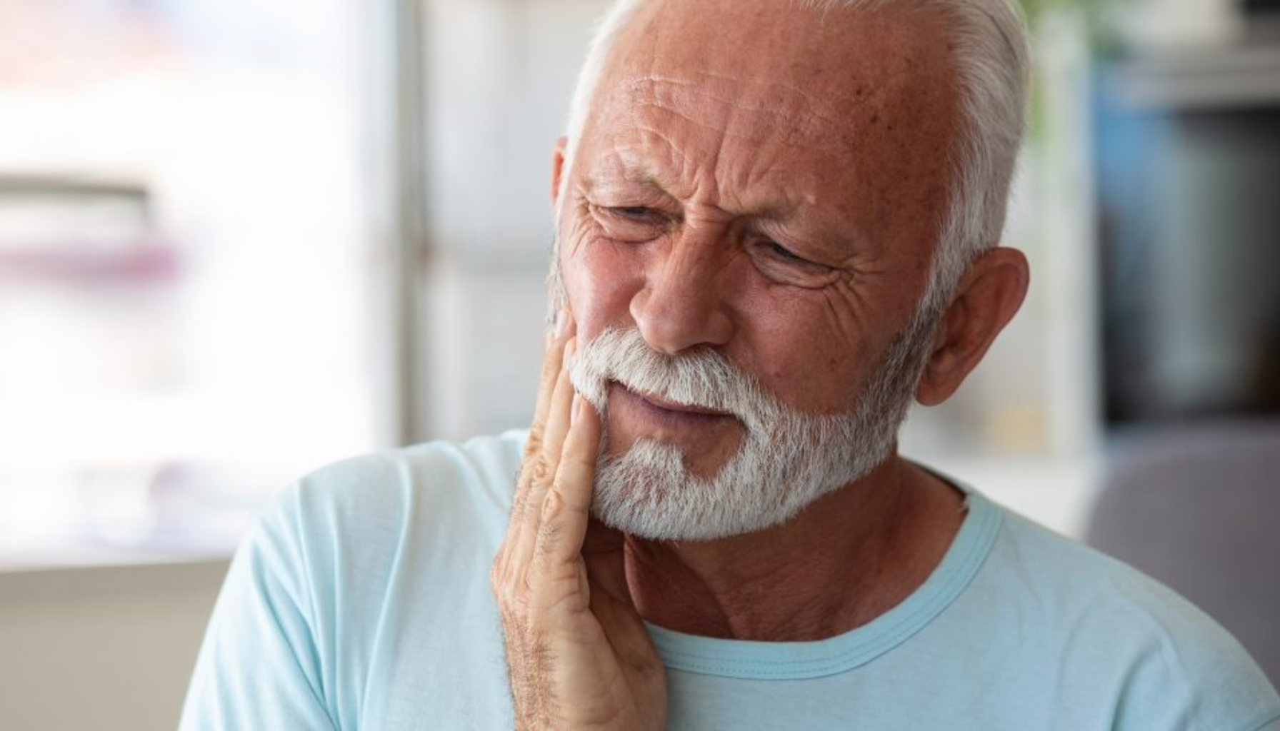 Eldre mann med smerte i kjeven holder seg til kinnet.