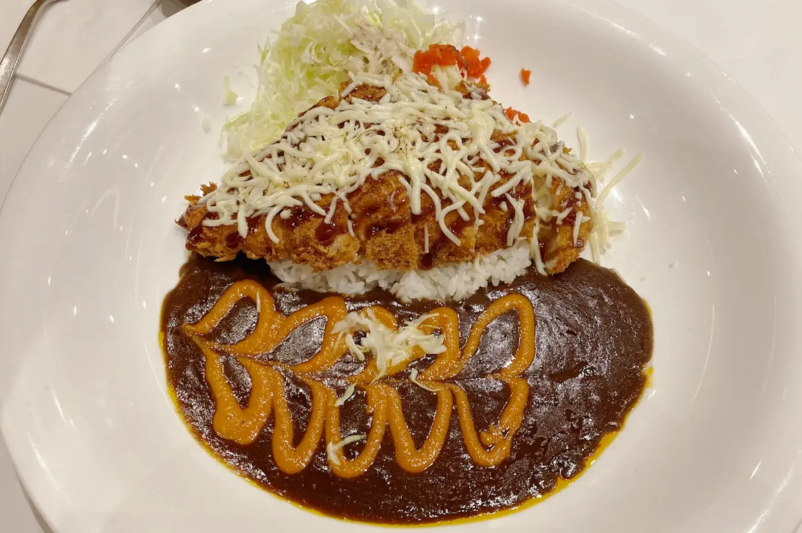 Creamy cheese-topped pork katsu served with a deep, savory Japanese curry sauce and shredded cabbage at Monster Planet, Singapore.