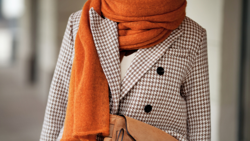 A person wearing an orange scarf and a houndstooth coat