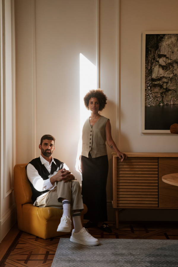 a man sits while a woman stands next to a piece of art in a living room