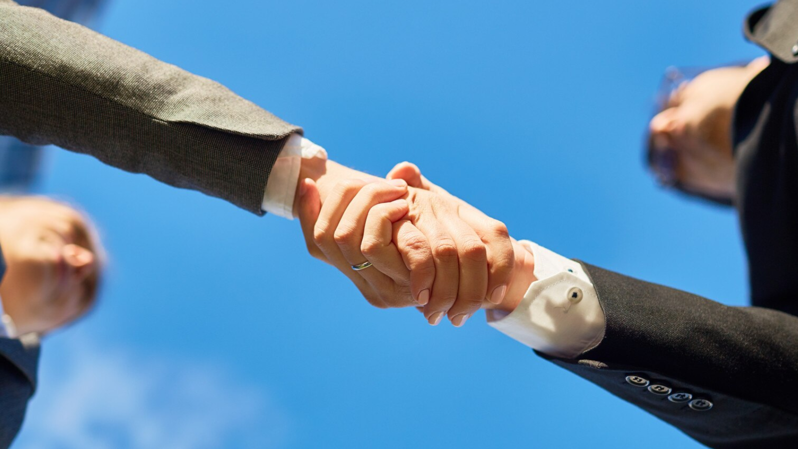 Close-up of two professionals in business attire shaking hands outdoors under a clear blue sky. The image symbolizes partnership and success in implementing modern phone systems and cloud-based communication like VoIP for scalable, cost-effective telecom services.