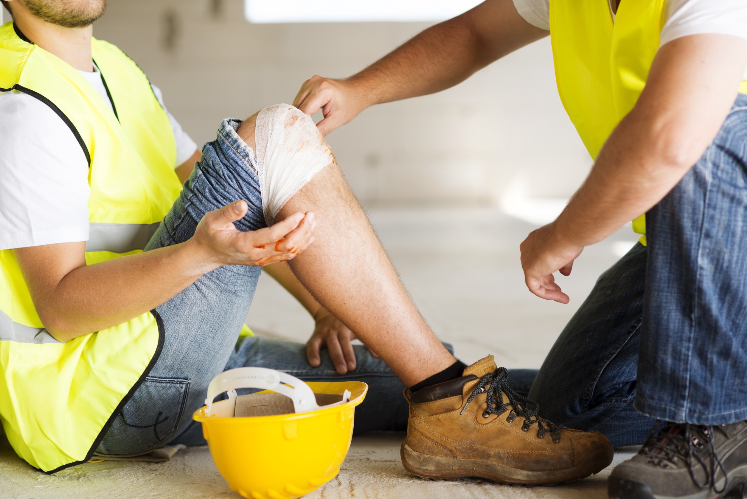 A warehouse worker with an injured knee receives medical treatment from a first aider 