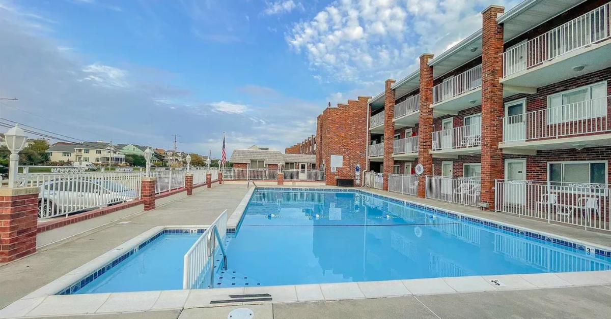 Outdoor heated pool at Cape Roc Rentals in Cape May, NJ, surrounded by brick buildings and private condo balconies.