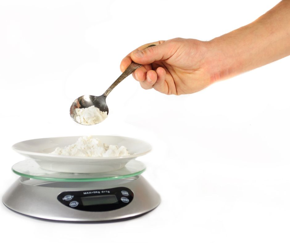 person spooning flour into a bowl of flour on a kitchen scale