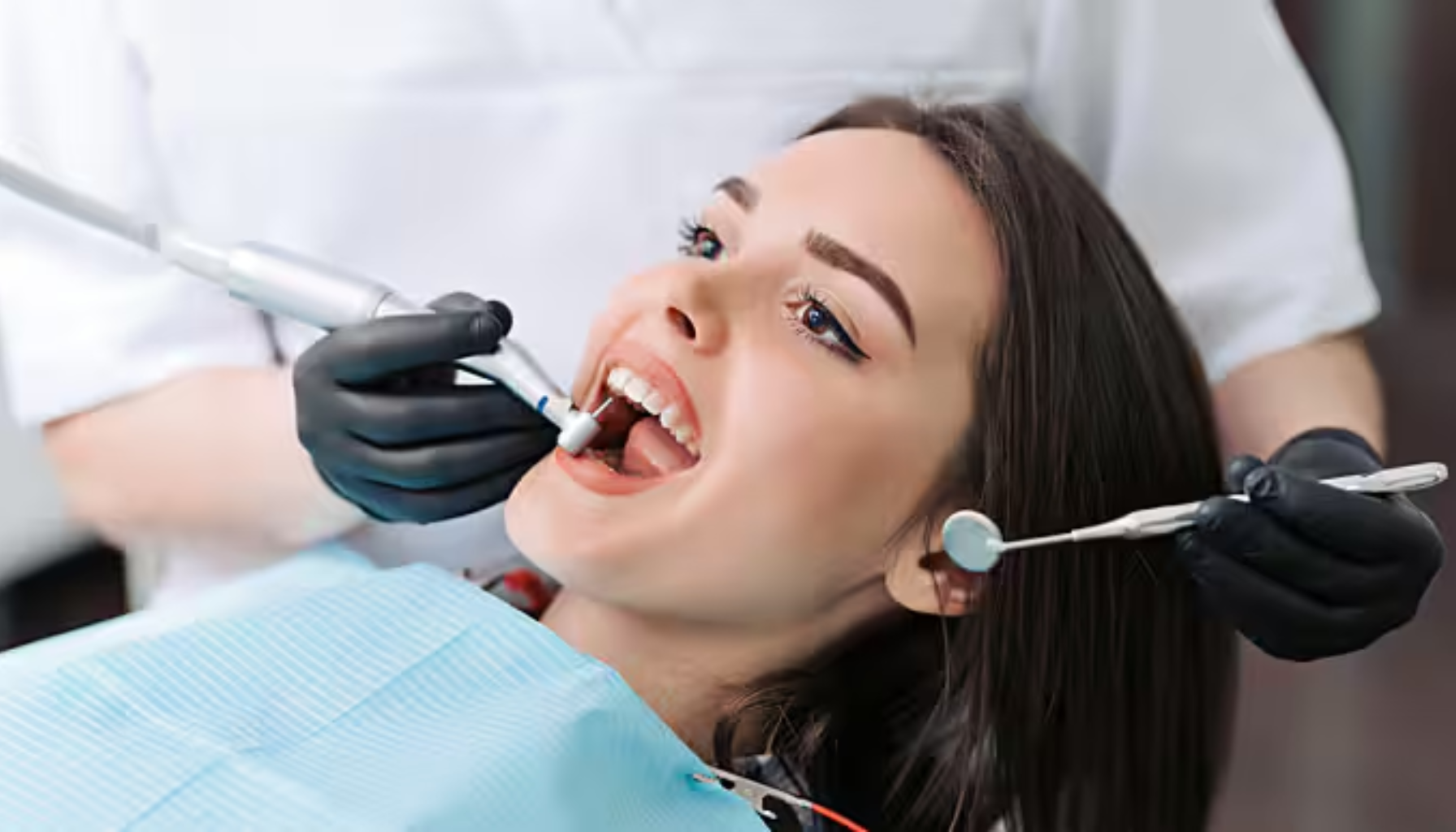 Kvinne får tannbehandling av tannlege med svarte hansker, som bruker speil og elektrisk instrument under undersøkelse.