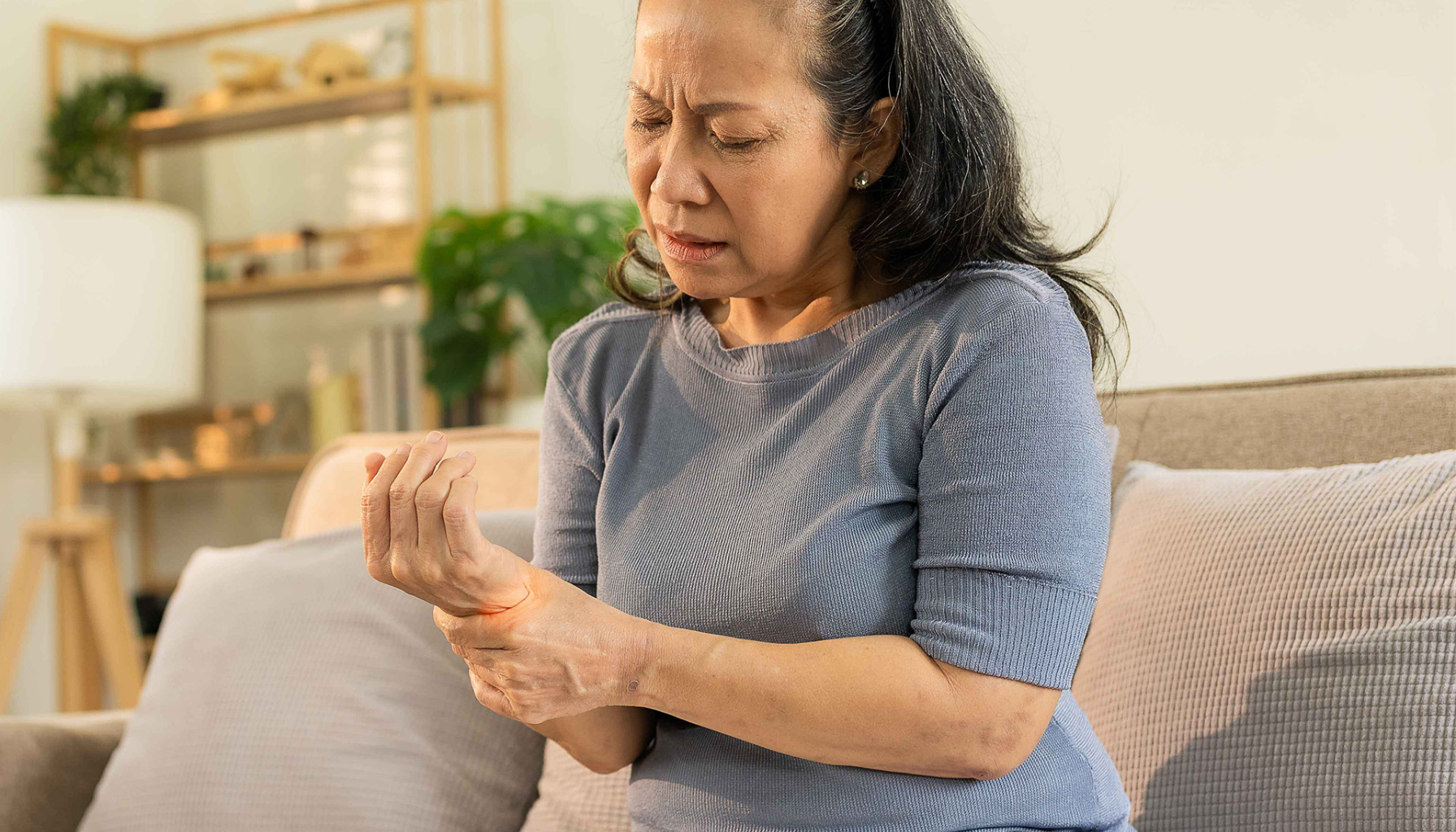 Kvinne med smertefullt uttrykk holder rundt håndleddet sitt, tydelig preget av ubehag eller nervesmerter i hånden.