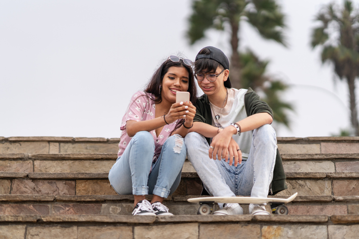 Two friends sitting on some steps and looking a cell phone. 