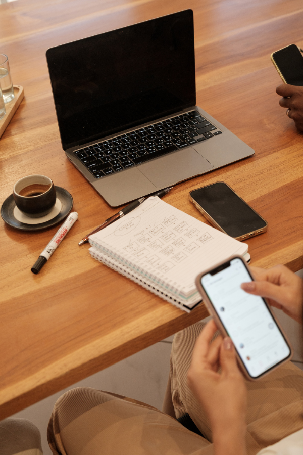 person sitting at a desk with a phone, laptop, and notebook creating an online course