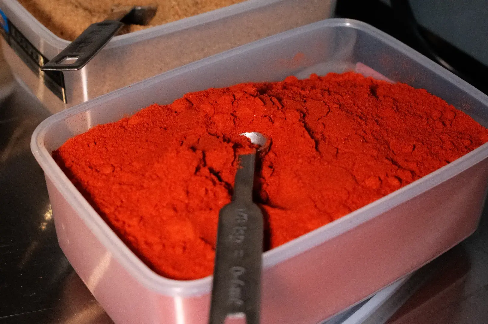 A container filled with red powder, likely a spice, with a measuring spoon resting on top.