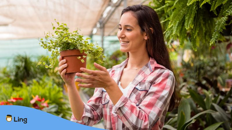 A photo of a smiling woman holding a plant inside a greenhouse.