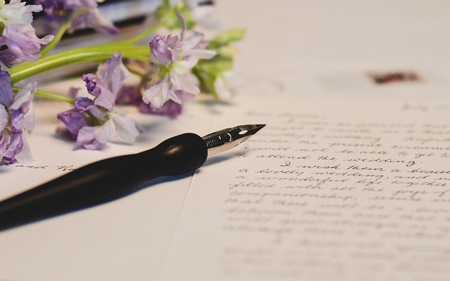 A fountain pen on a page, next to purple flowers representing the idea of famous writing.