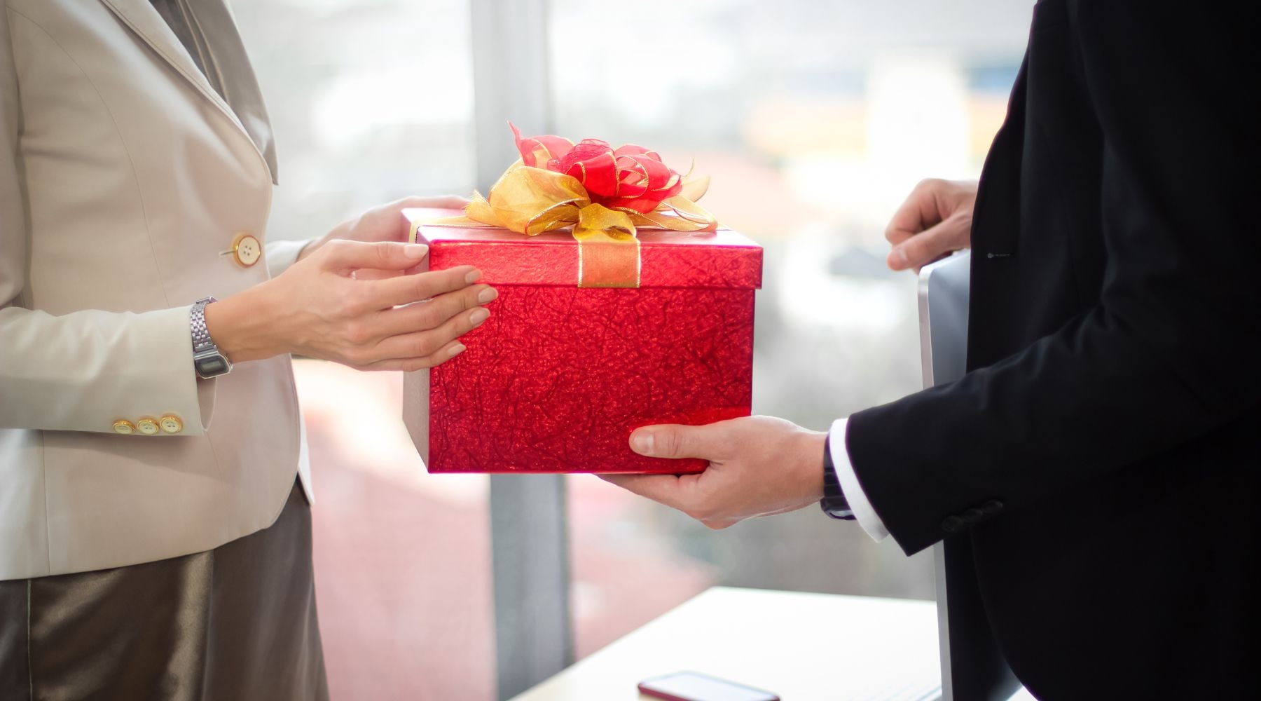 Business people exchanging a red gift box, symbolizing corporate gifting.