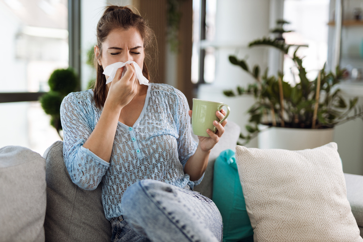 An image of a woman with seasonal allergies blowing her nose. 