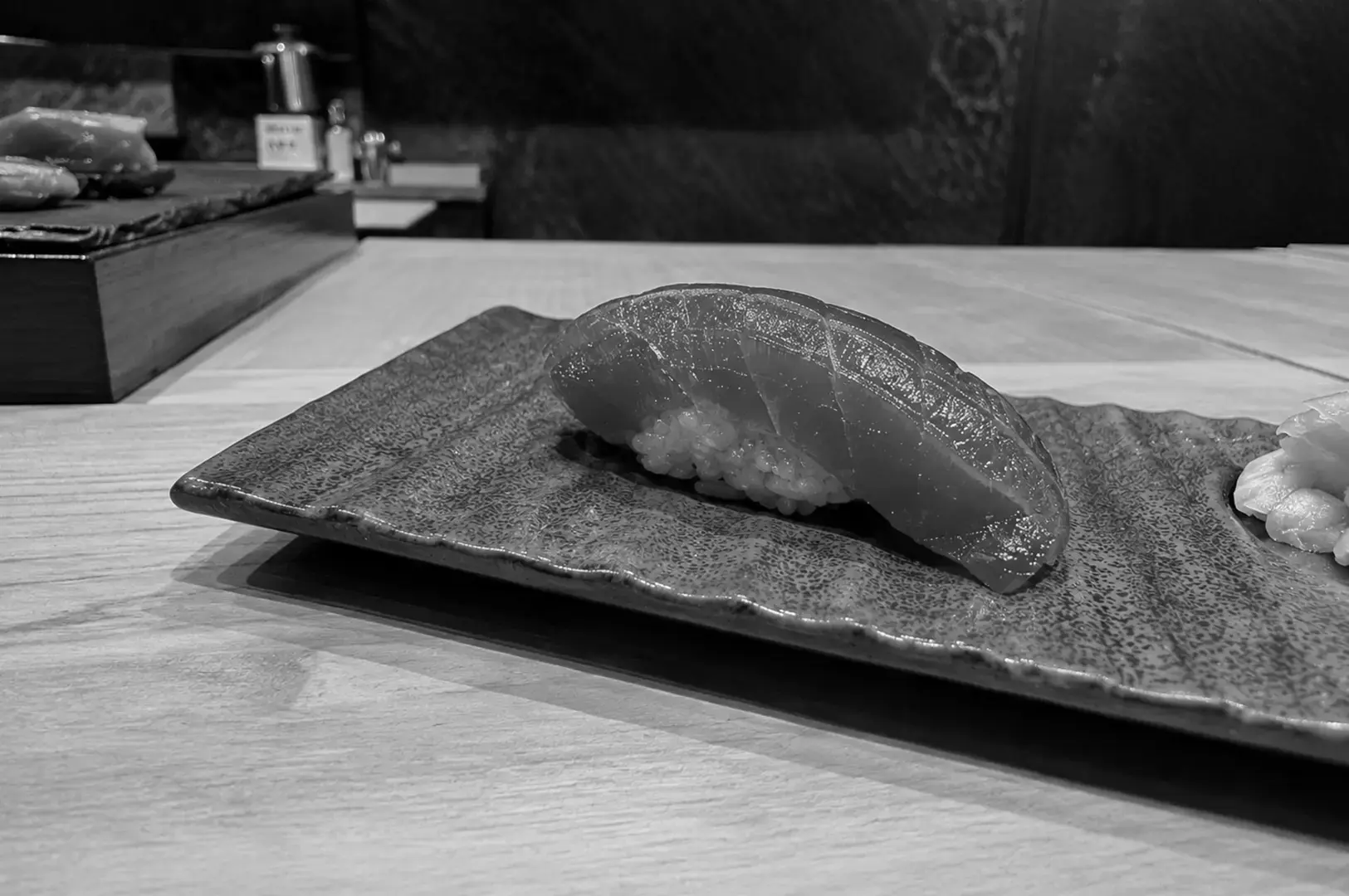 Fresh tuna nigiri sushi served on a textured ceramic plate at a sushi counter.