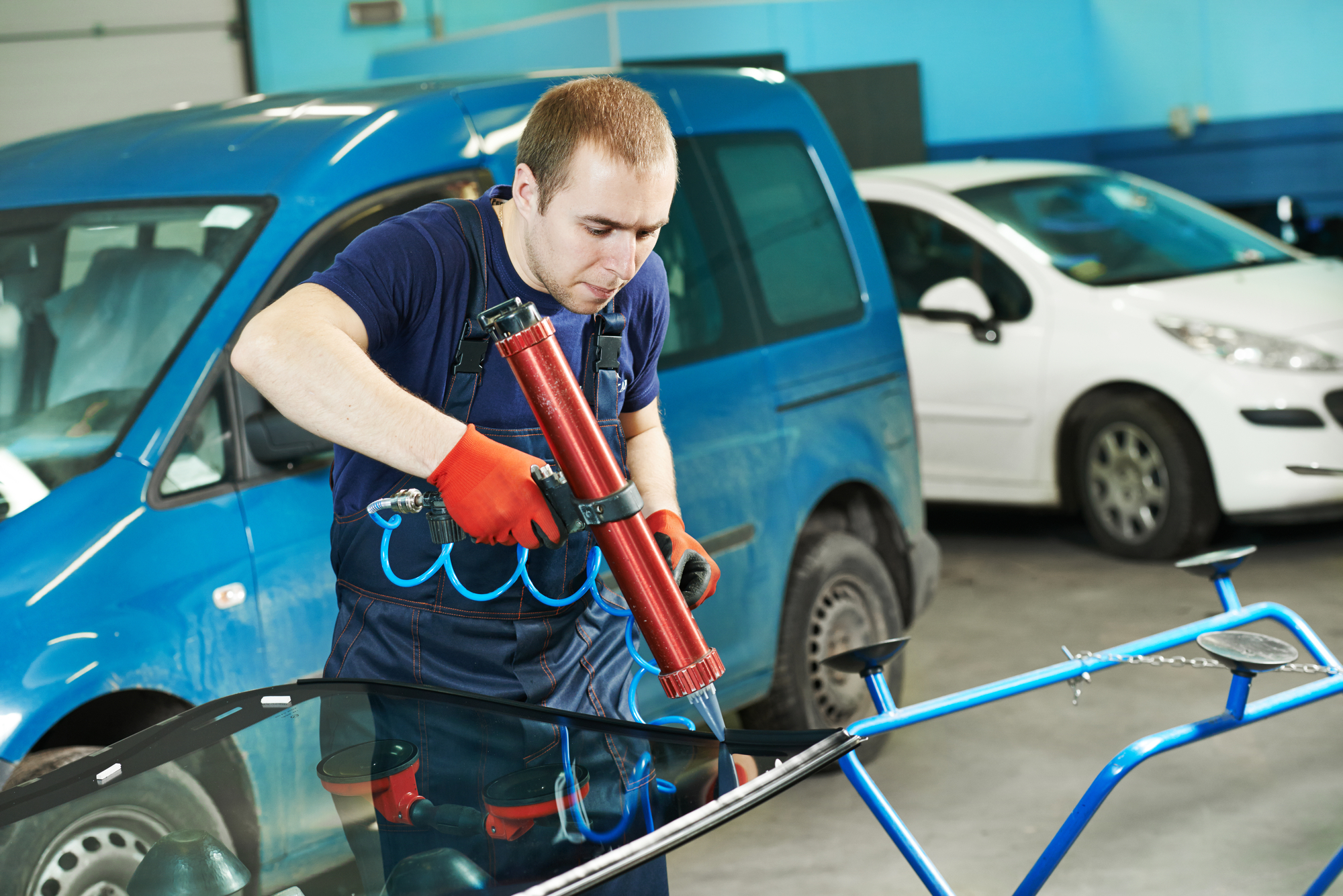 Car glazier applying new glue on a windshield in shop